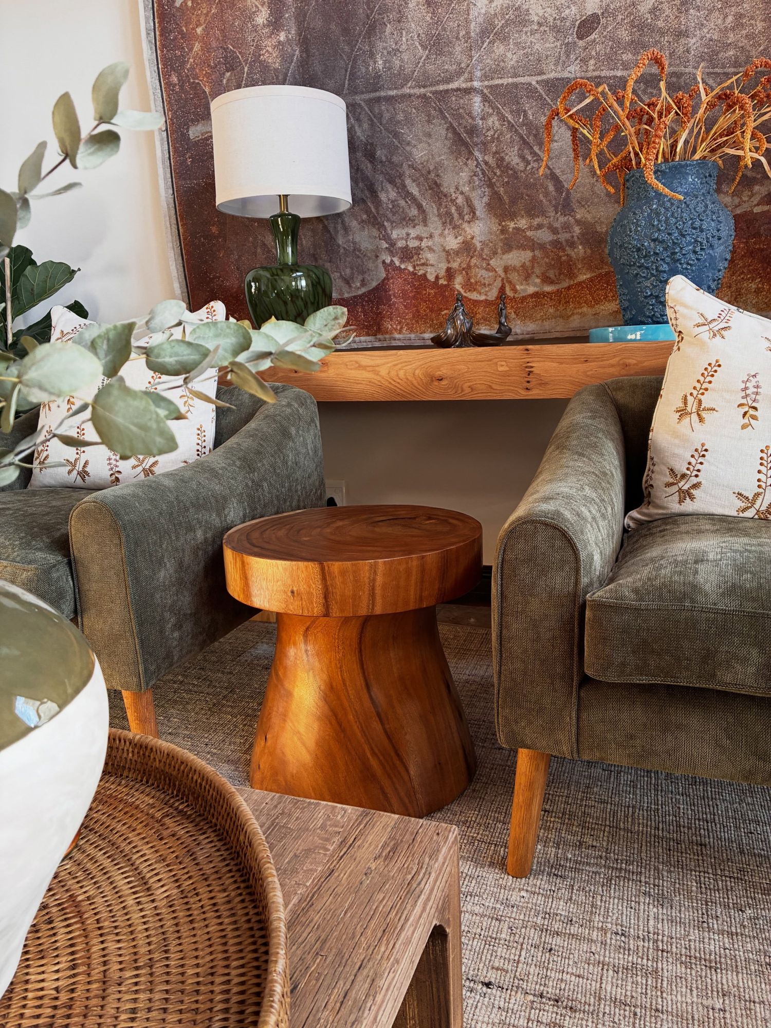 A styled corner: armchairs, a timber stool, a lamp and flowers